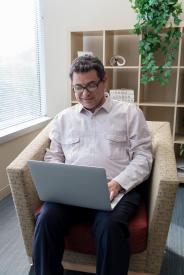 image tagged with sits, man, sit, glasses, typing, …;