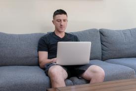 image tagged with man, looks, couch, computer, looking, …;